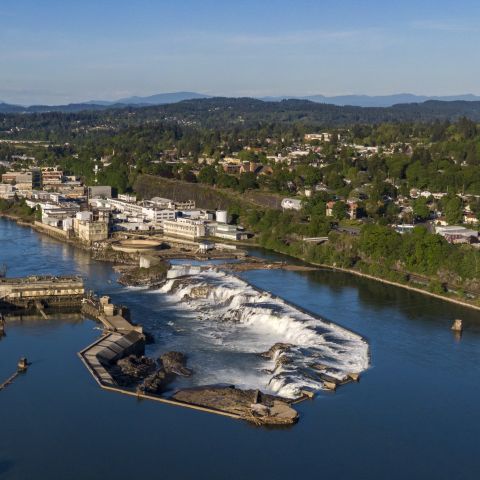 aerial view of deep blue river water at falls on the edge of a verdant cityscape