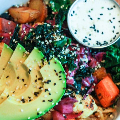 a bowl of brightly colored vegetables with avocado slices on top and a dressing on the side