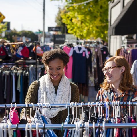 two people look through outdoor racks of clothing on a sunny day