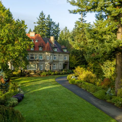 A large stone mansion with red roof surrounded by trees