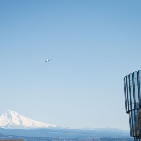 a plane takes off through clear blue skies with a snowy mountain in the distance and a control tower in the foreground