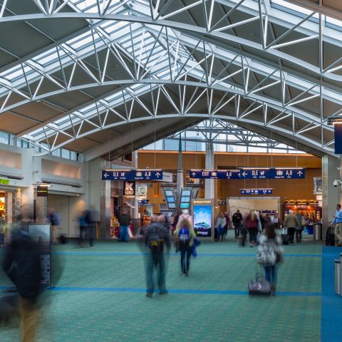 travelers out of focus walk through an airport concourse over green carpet