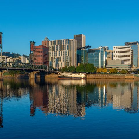 calm river water reflects the buildings in a downtown area that are catching the sunrise on a clear day