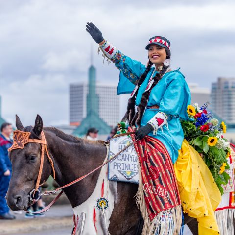native american woman on colorfully decorated horse waves in parade
