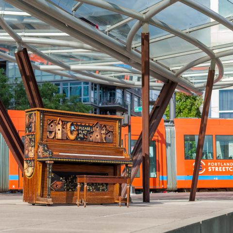 decorated paint reads please play me at a metro stop as an orange street car passes behind