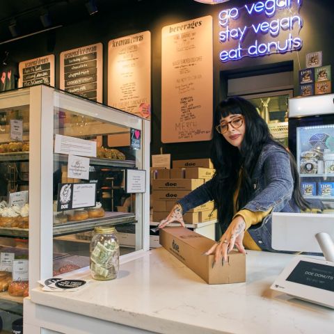 a woman at a counter closes the lid on a box of doughnuts