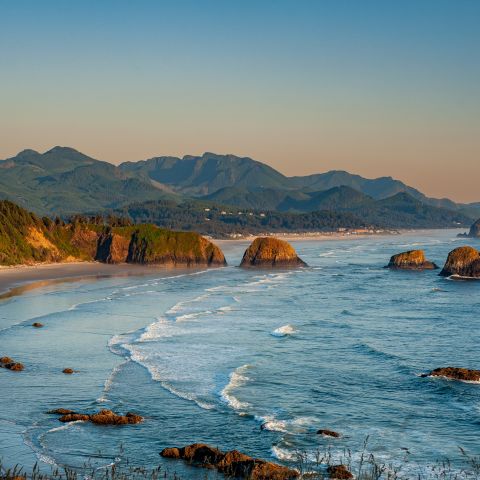 an aerial view of the Oregon Coast with the coast mountain range in the background, a sea of green