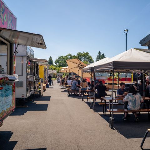 a row of food carts and diners enjoying covered outdoor seating on a sunny day