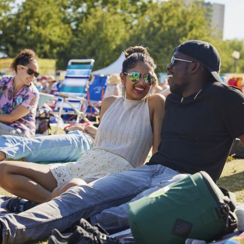 two people sit together in the sunshine in the middle of a crowd