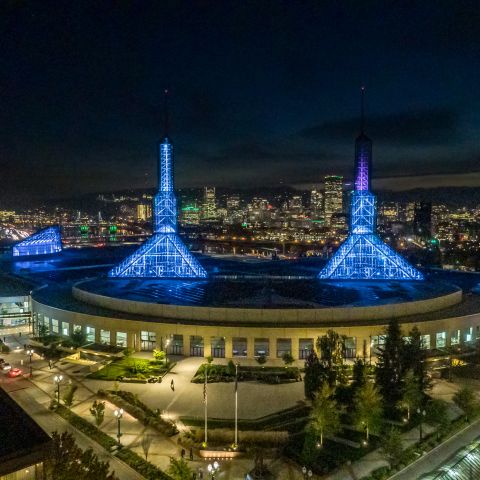 a vast building with two blue spires at night with the bright city skyline in the background