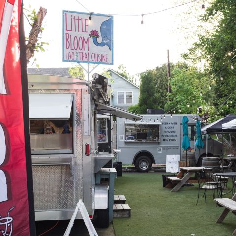 A food cart pod with food trucks gathered around a small seating area with picnic tables.