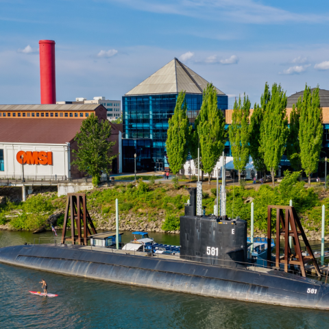 the exterior view of OMSI beside the Willamette River with a submarine docked by a pier.