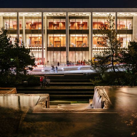 exterior of the Keller Auditorium at night showing a wide building lit from within, viewed from the Keller Fountain, whose geometric lines mirror the auditorium\'s architecture