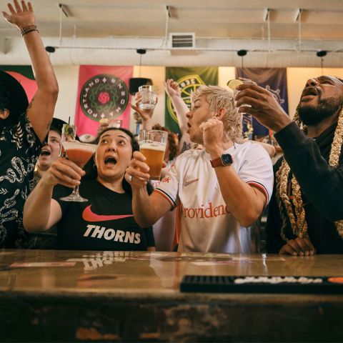 a crowd of people cheer while raising glasses in front of a bar while watching a game