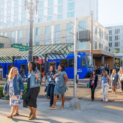 Group of people walking across the street with light rail in the background
