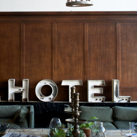 two people sit on a couch in front of \'hotel\' sign while another person stands behind a counter