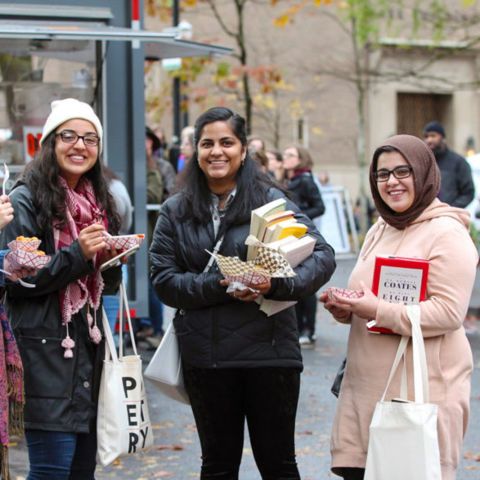 three people standing near a food cart carrying books