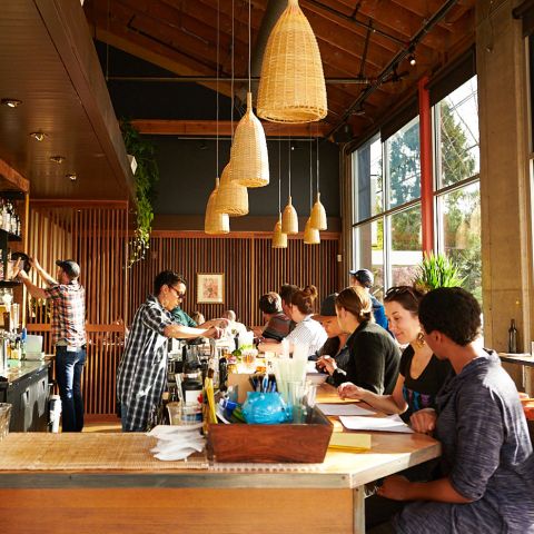 two bartenders make drinks while customers sit at bar looking at a menu