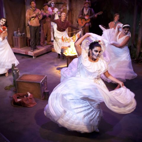 Actors dancing across a stage in long white dresses and skeleton makeup