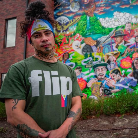 Talilo Marfil, wearing the flag of the Philippines as bandana and a shirt with the word, \'flip,\' (a slang term for Filipino) stands in front of a colorful mural depicting his likeness.