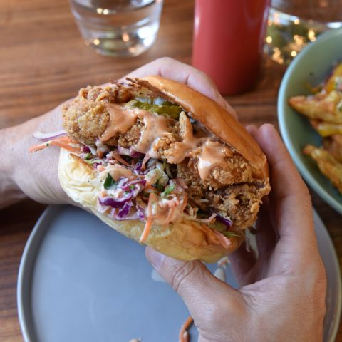 two hands hold up a delectable fried chicken sandwich complete with sauce and veggies