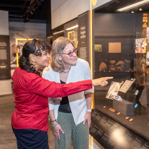 two women smile while looking at a historical display
