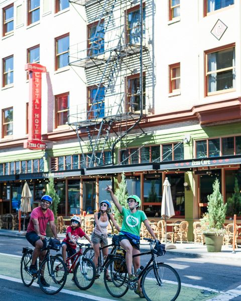 family on bikes stop in green bike lane, one pointing up with building towering behind them in cityscape