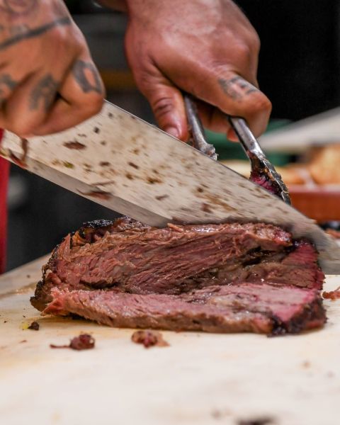 a close-up of a chef cutting slices of juicy brisket