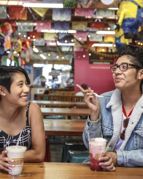 Two smiling people sit at a wooden table in a brightly decorated interior