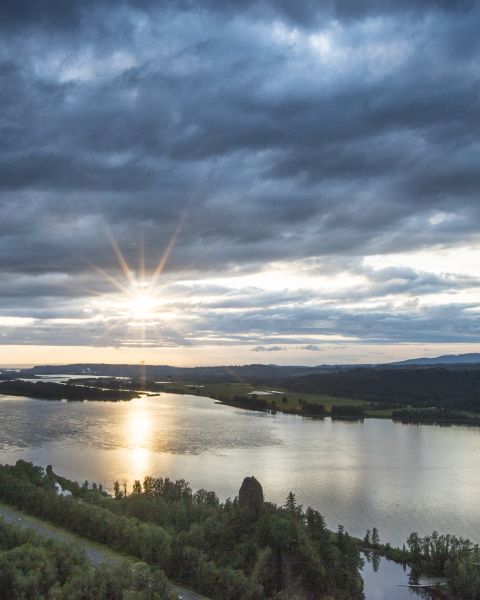 The sun breaks through clouds above a wide river