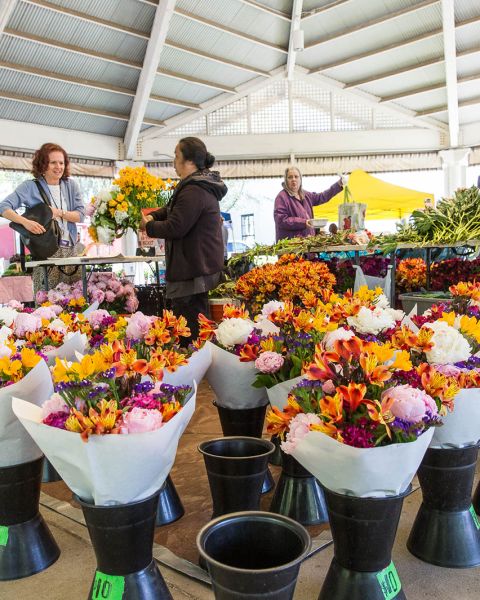 flower vendor standing in the middle of many colorful bouquets selling a single bouquet to a customer at a farmers market