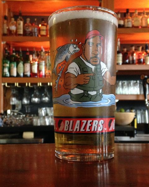 a vintage Portland Trail Blazers glass sits on a bar with rows of bottles behind it