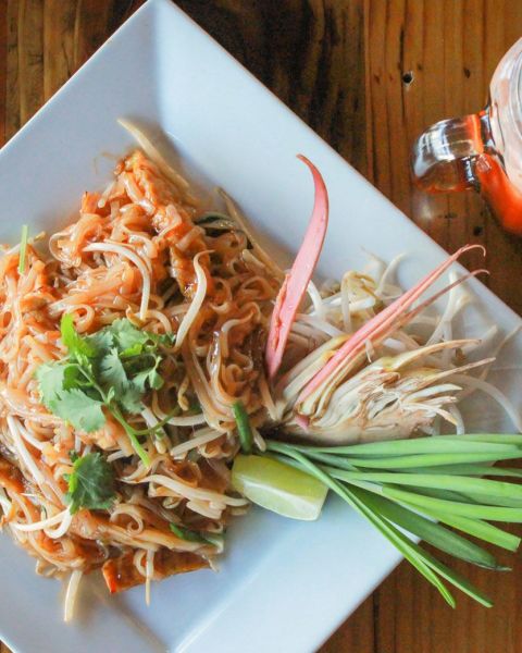 a close-up of a plate of Thai food and Thai iced tea