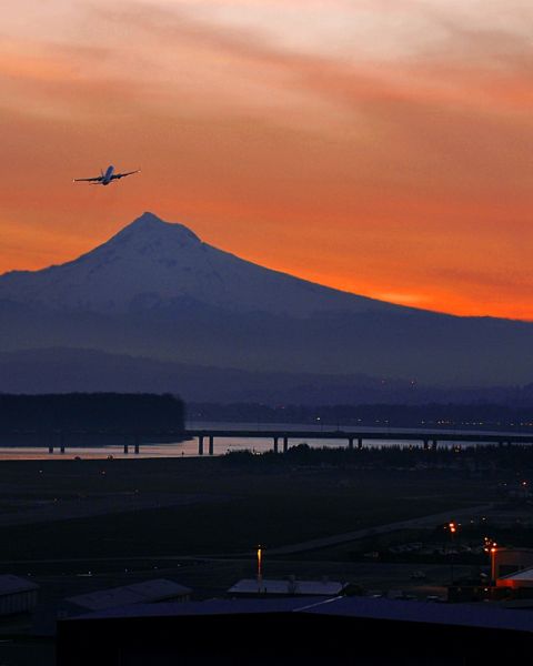 the silhouette of a plane against an orange sunset with Mount Hood in the background