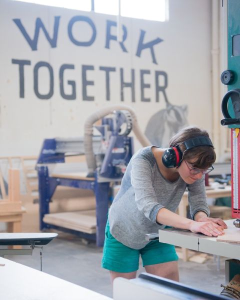 a person uses a large band saw to cut wood in a woodworking shop