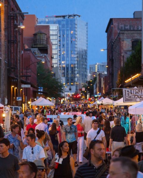 a twilight street filled with people browsing tents with items on display