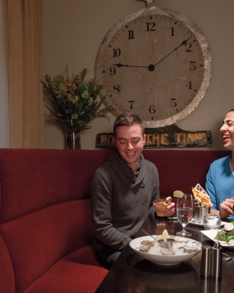 a couple laughing over dinner and drinks in a red corner booth