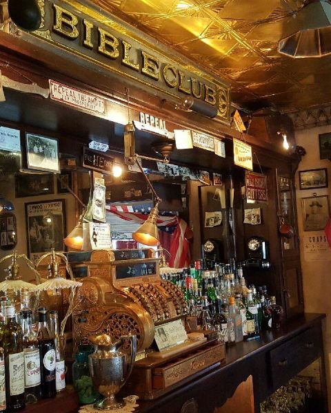 an old, golden cash register on a bar countertop with bottles and a large mirror on the back wall