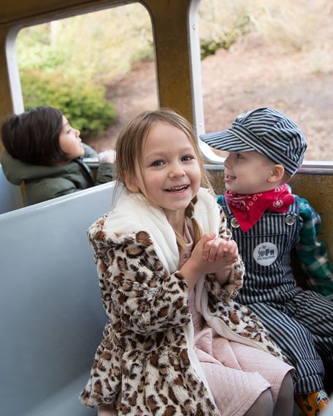 two children sitting on a train, one is dressed like a train conductor