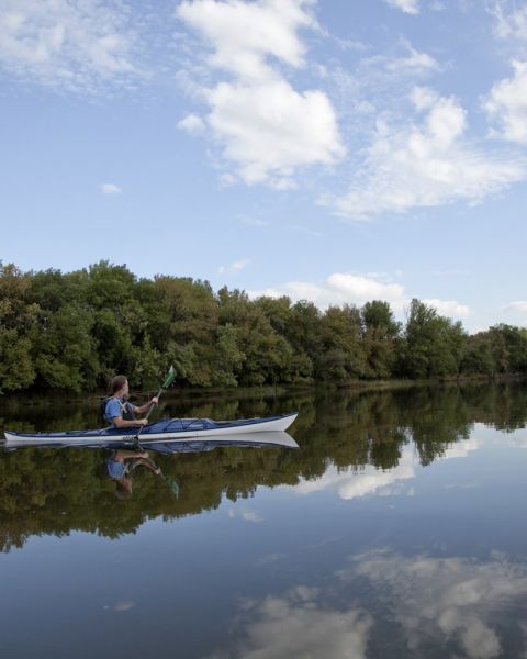 a person kayaking on glassy water with puffy clouds reflected in it