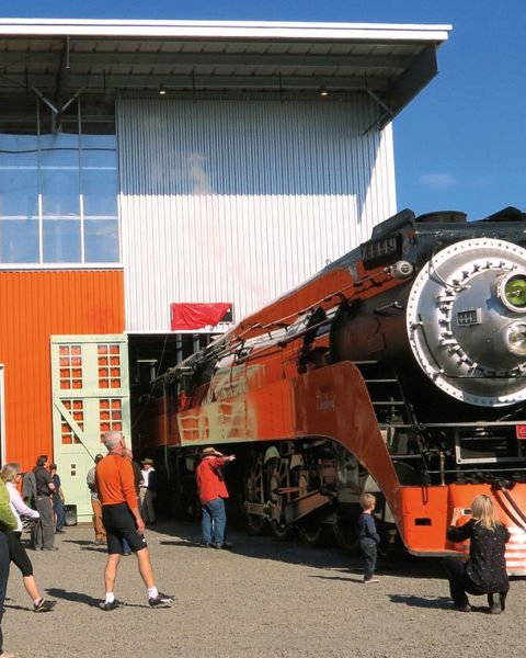 Many people are admiring a bright orange steam engine at the Oregon Rail Heritage Center.