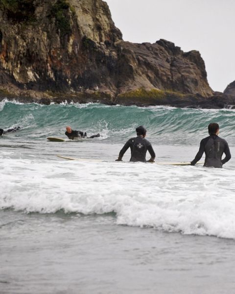 Surfers at Oswald West State Park on the Oregon Coast, with a large rock structure in the background