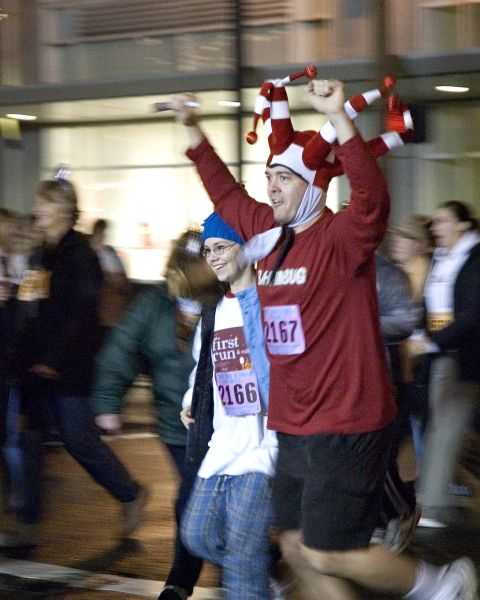 a man in a joker hat is among a crowd of people running in a fun run for new year\'s eve