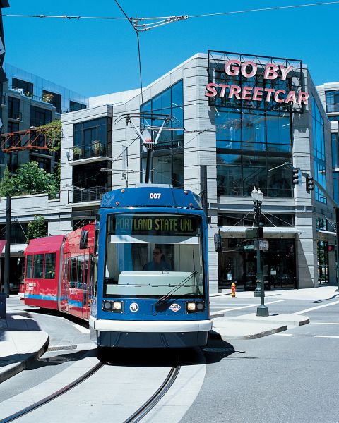 A streetcar passes by a large, red sculpture in front of a building with a neon sign reading, \"Go By Streetcar.\"