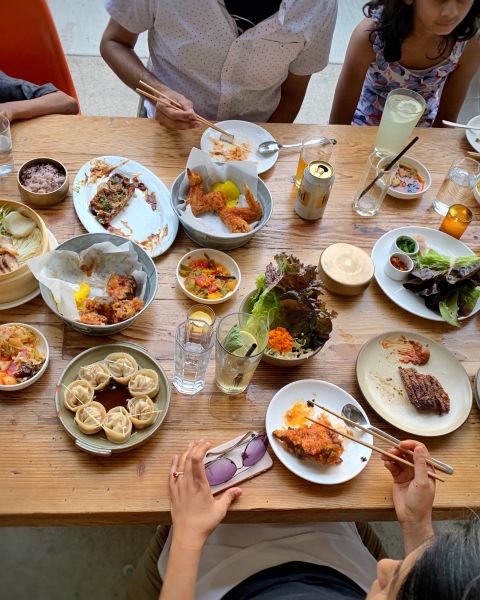 people sit around a vast spread of Korean food arrayed on a wooden table