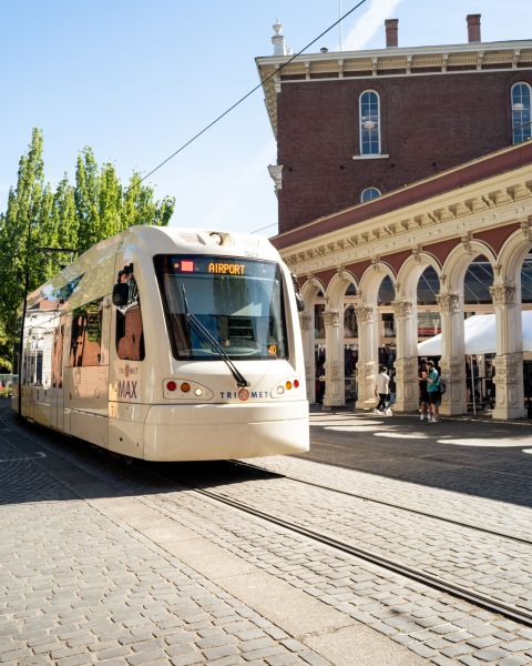 Light rail train car driving past people shopping at an outdoor market