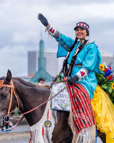 native american woman on colorfully decorated horse waves in parade