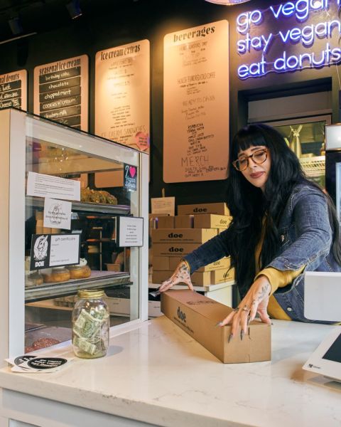 a woman at a counter closes the lid on a box of doughnuts