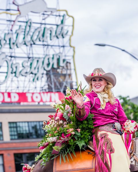 woman riding a horse adorned with roses waves during a parade in downtown Portland