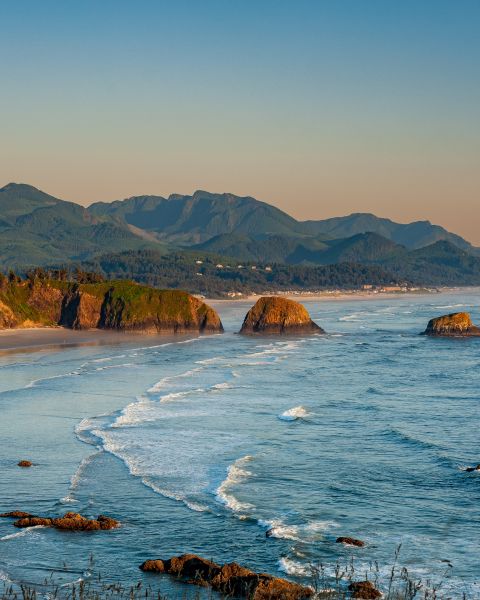 an aerial view of the Oregon Coast with the coast mountain range in the background, a sea of green